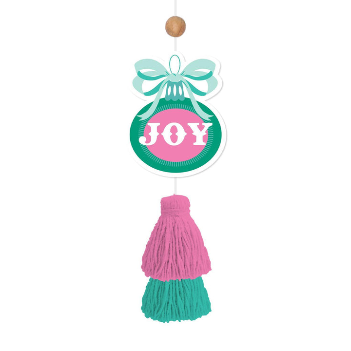 Ornament-shaped car air freshener with a light blue bow, a teal circular base with a pink “JOY” center, and a pink and teal yarn tassel.