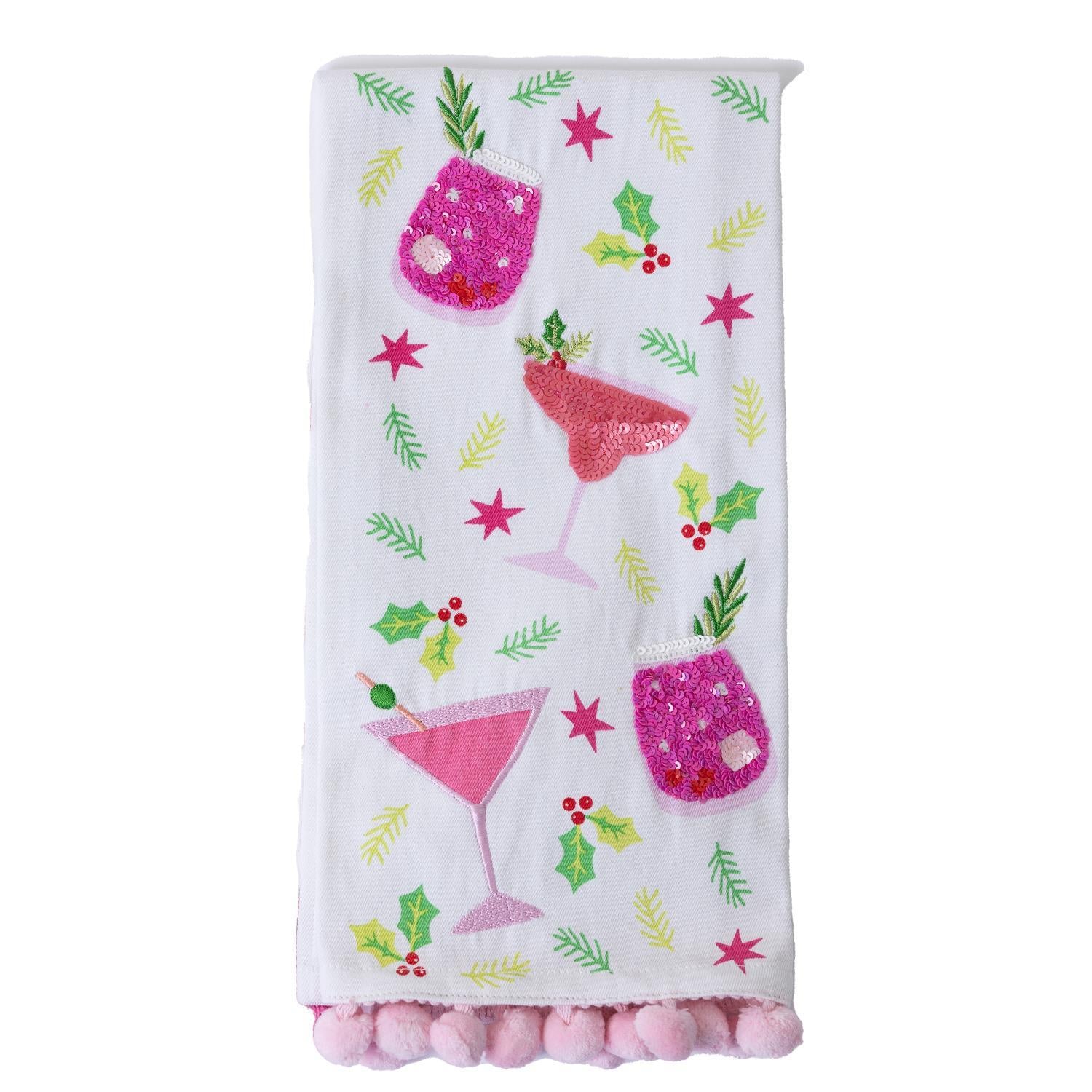 The Festive Christmas Tea Towel features pink cocktails, holly leaves, berries, stars, and a pink pom-pom trim at the bottom. Available size: 18" x 28".