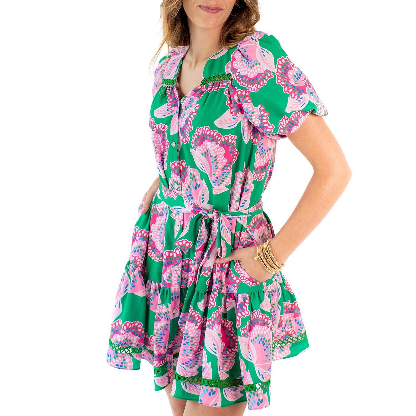 The Addison Petal Tango Dress is a green dress with pink and white floral patterns. It features a removable tie belt, short bubble sleeves, and pockets. Available in sizes XS to XL.