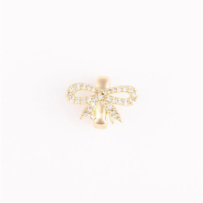 Gold bow-shaped bracelet charm with clear stones. Elegant, timeless design. Available sizes: S, M, L.