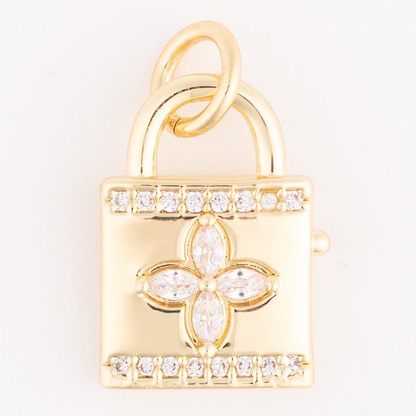 The Thea Charm Bar is a gold padlock charm with a central floral diamond motif and two rows of diamonds on the top and bottom. Hypoallergenic, fits any 18k gold plated necklace. Available sizes: Small, Medium, Large.
