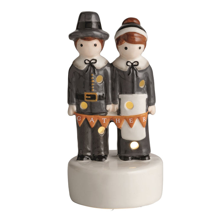Ceramic Pilgrim LED Sitter featuring a man and woman in classic attire on a white base with “GATHER” banner; illuminated sections. Available in standard tabletop size.