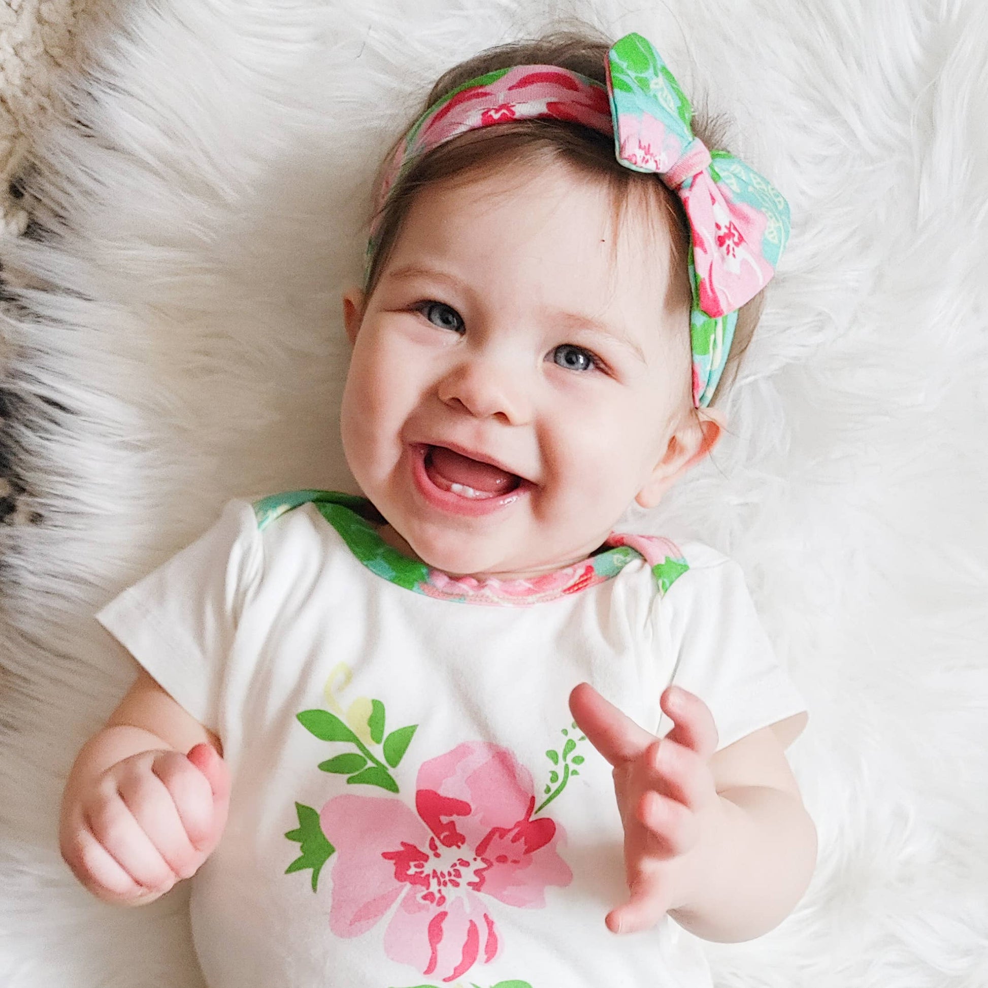 baby modeling onesie and headband laying on a faux fur rug. Baby is smiling.