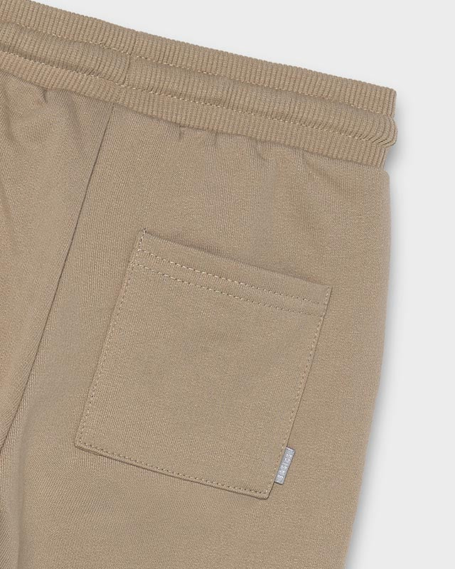 Close-up of hazelnut brown Baby Jogger Pants showing ribbed elastic waistband and stitched square back pocket with small white tag; available in sizes 0-3M, 3-6M, 6-12M, and 12-18M.