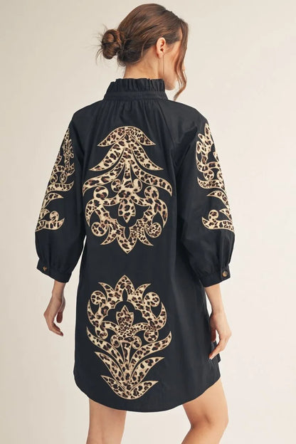 Black Baroque Button Up mini dress with long sleeves, featuring large tan and gold ornate floral patterns on the back and sleeves. Available in sizes XS–XL.