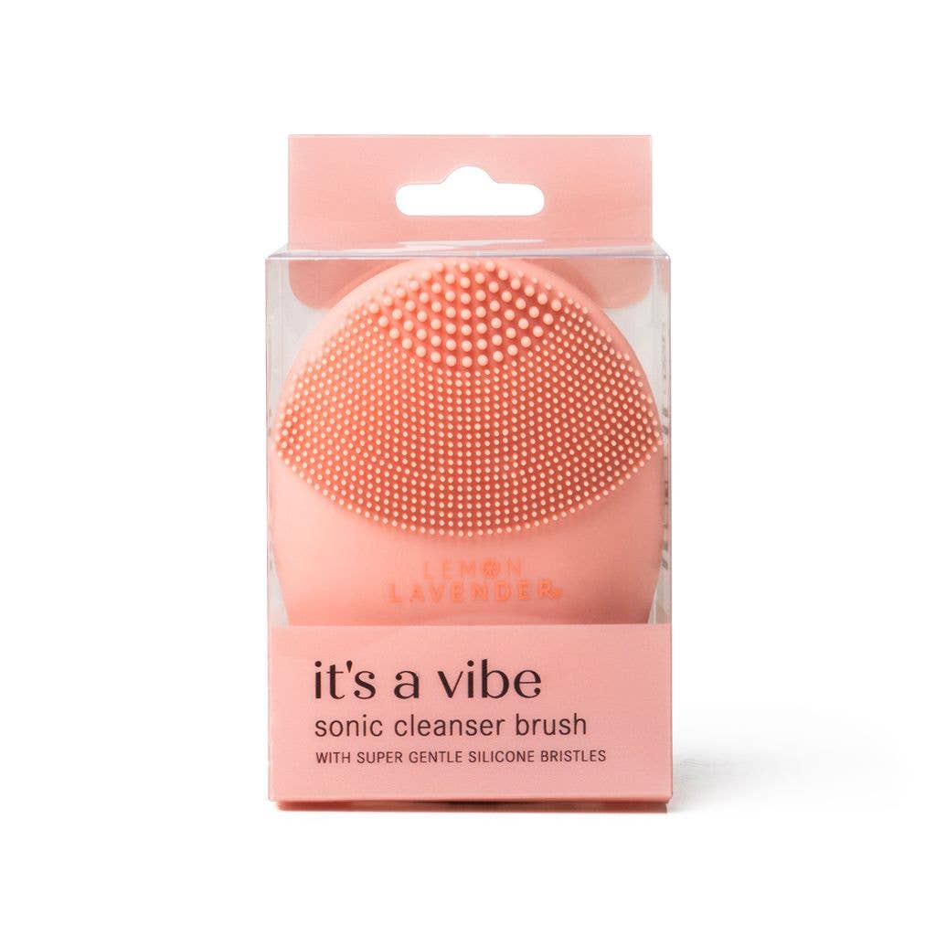 Pink, round silicone sonic cleanser brush in clear packaging labeled “it’s a vibe,” available in one compact size.