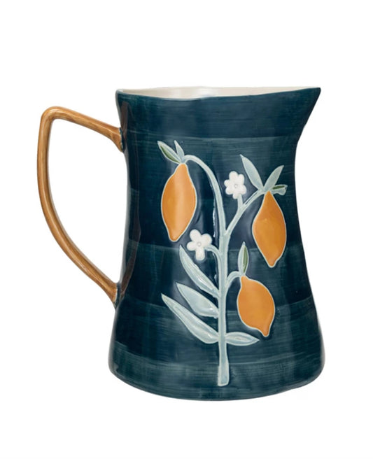 This product is a 3 Quart Stoneware Pitcher, hand-painted and finished in glossy dark blue. It features an artistic design of a lemon tree branch with yellow lemons and white wax relief flowers. The handle has been painted in a contrasting brown color for differentiation.