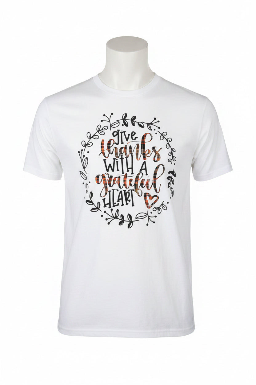 Give Thanks with a Grateful Heart T-Shirt features the phrase “give thanks with a grateful heart” in elegant lettering, encircled by a black leafy wreath and accented with a small heart. Available in sizes S–XXL.