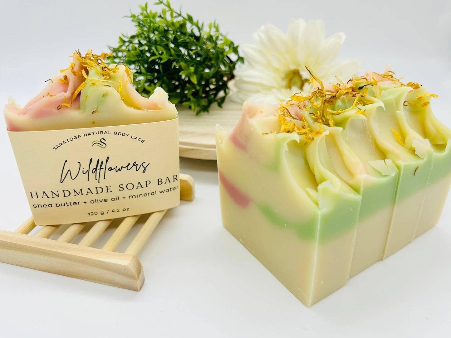 Handmade vegan cold process soap bars with swirls of pastel yellow, pink, and green. Each bar is topped with dried flowers and individually labeled "Wildflowers floral soap bar.