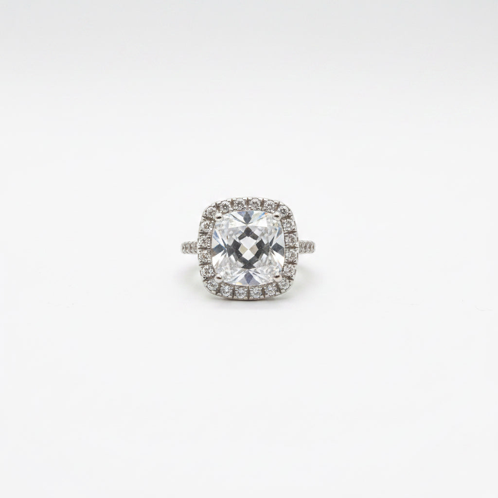 Midgle Silver Crystal Statement Ring with a cushion-cut crystal, halo of smaller stones, pavé band, and silver-tone finish. Available in sizes 6-9.