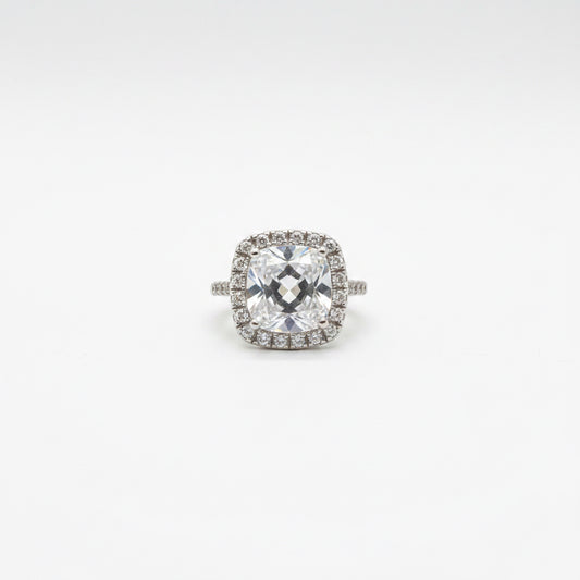Midgle Silver Crystal Statement Ring with a cushion-cut crystal, halo of smaller stones, pavé band, and silver-tone finish. Available in sizes 6-9.