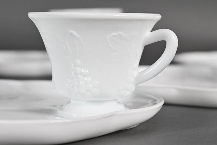 White milk glass teacup with grapevine pattern on matching saucer. Available in 6-oz cup and 7-inch plate sizes.