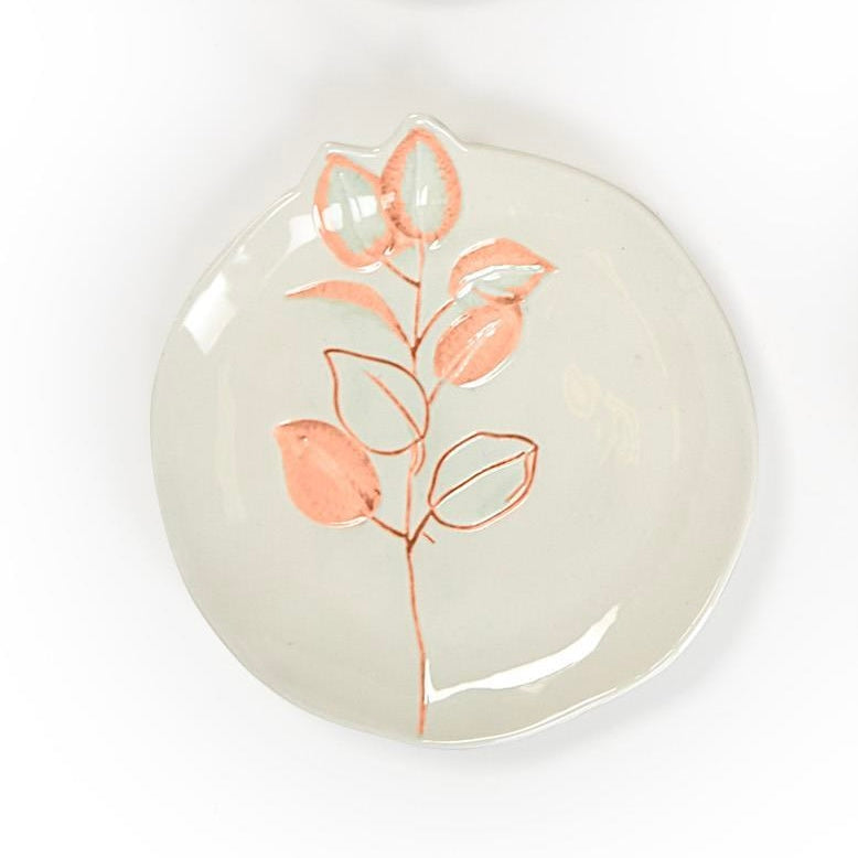 Round off-white stoneware plates with peach branch design; uneven organic shape. Available in small and medium sizes.
