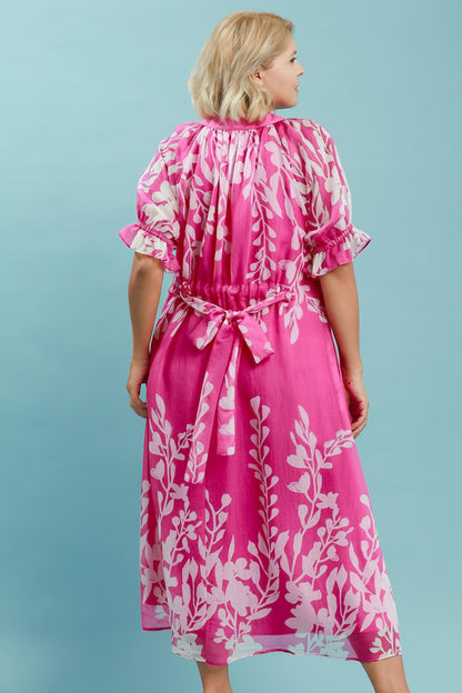 Pink floral midi dress with white patterns, short ruffled sleeves, tied waist sash, and split V-neckline. Available in sizes XS-XL.