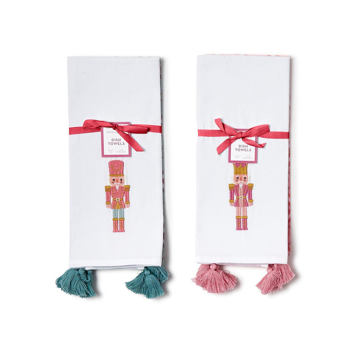 Nutcracker set of two white festive dish towels with ribbons, embroidered nutcrackers, and tassels.