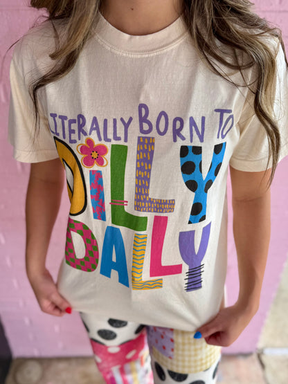 Cream garment-dyed cotton tee with "Literally Born to Dilly Dally" graphic. Sizes: Youth XS–XL, Adult S–3XL.