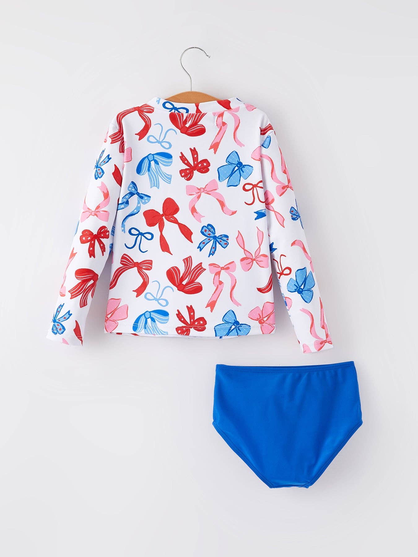Long-sleeve white rash guard with red and blue bow prints, solid blue bottoms. Sizes: 2T-5T.