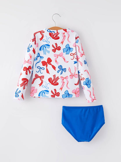 Long-sleeve white rash guard with red and blue bow prints, solid blue bottoms. Sizes: 2T-5T.