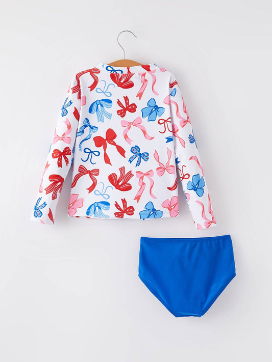 Long-sleeve white rash guard with red and blue bow prints, solid blue bottoms. Sizes: 2T-5T.