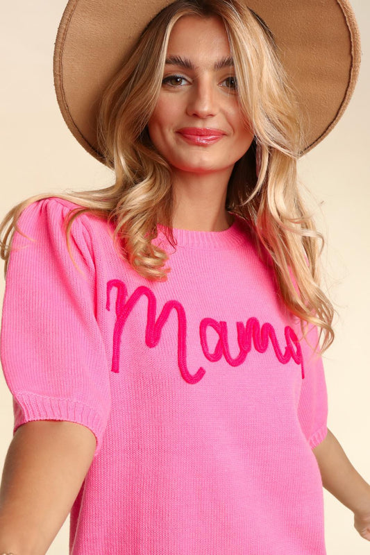 A woman wearing a pink Mama Embroidered Pop Letter Short Bubble Sleeve sweater and a beige hat smiles gently at the camera. Her blonde hair is styled in soft waves.