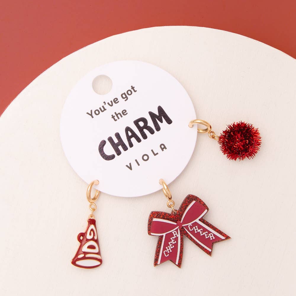 Charm Set with pom pom, megaphone, and glittered bow on a card. Sizes: one size.