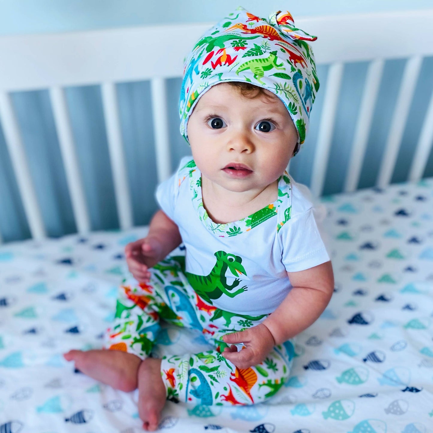 Baby modeling the whole set sitting in a white crib in a blue room 