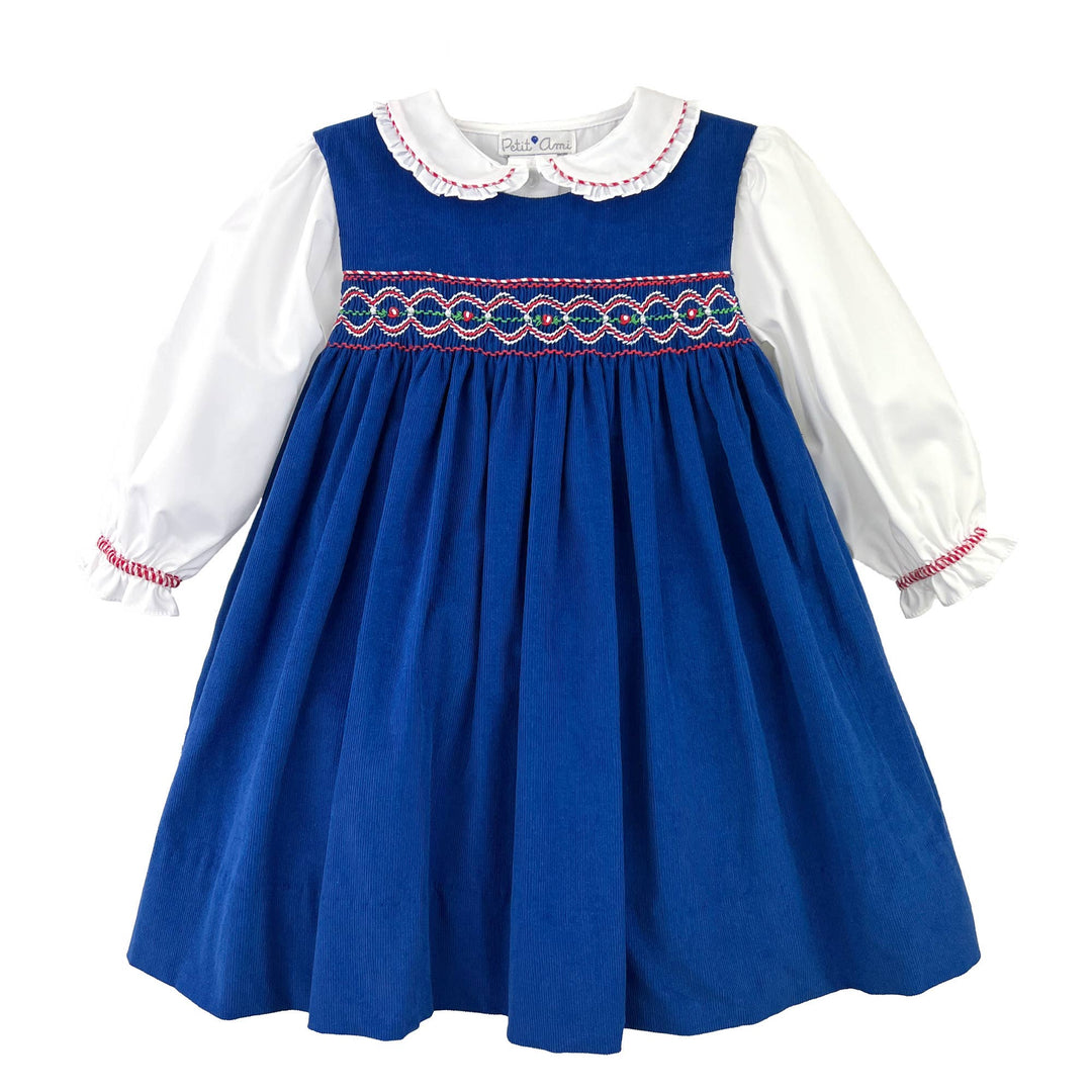 Navy corduroy smocked jumper dress with long white sleeves, ruffled collar, and embroidered chest. Sizes available.