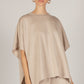 A woman in a P. CILL Butter Modal Side Slit Cape Top with sizing details and matching pants, stands with her hair pulled back and hoop earrings.