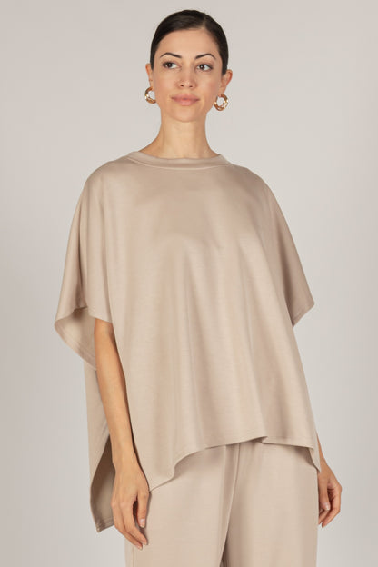 A woman in a P. CILL Butter Modal Side Slit Cape Top with sizing details and matching pants, stands with her hair pulled back and hoop earrings.