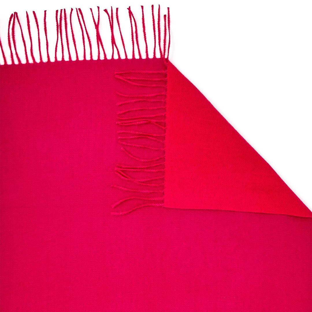 Bright pink rectangular reversible scarf with fringe on one edge, folded to show a different pink shade. Sizes: S, M, L.