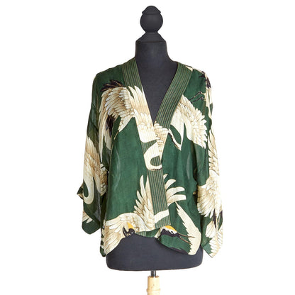Heron Print Forest Green Short Kimono: A jacket-style blouse with wide sleeves and a deep V-neckline trimmed with stripes. Made from sustainable materials, it features an elegant heron print in cream and beige tones. Sizes available: S, M, L.
