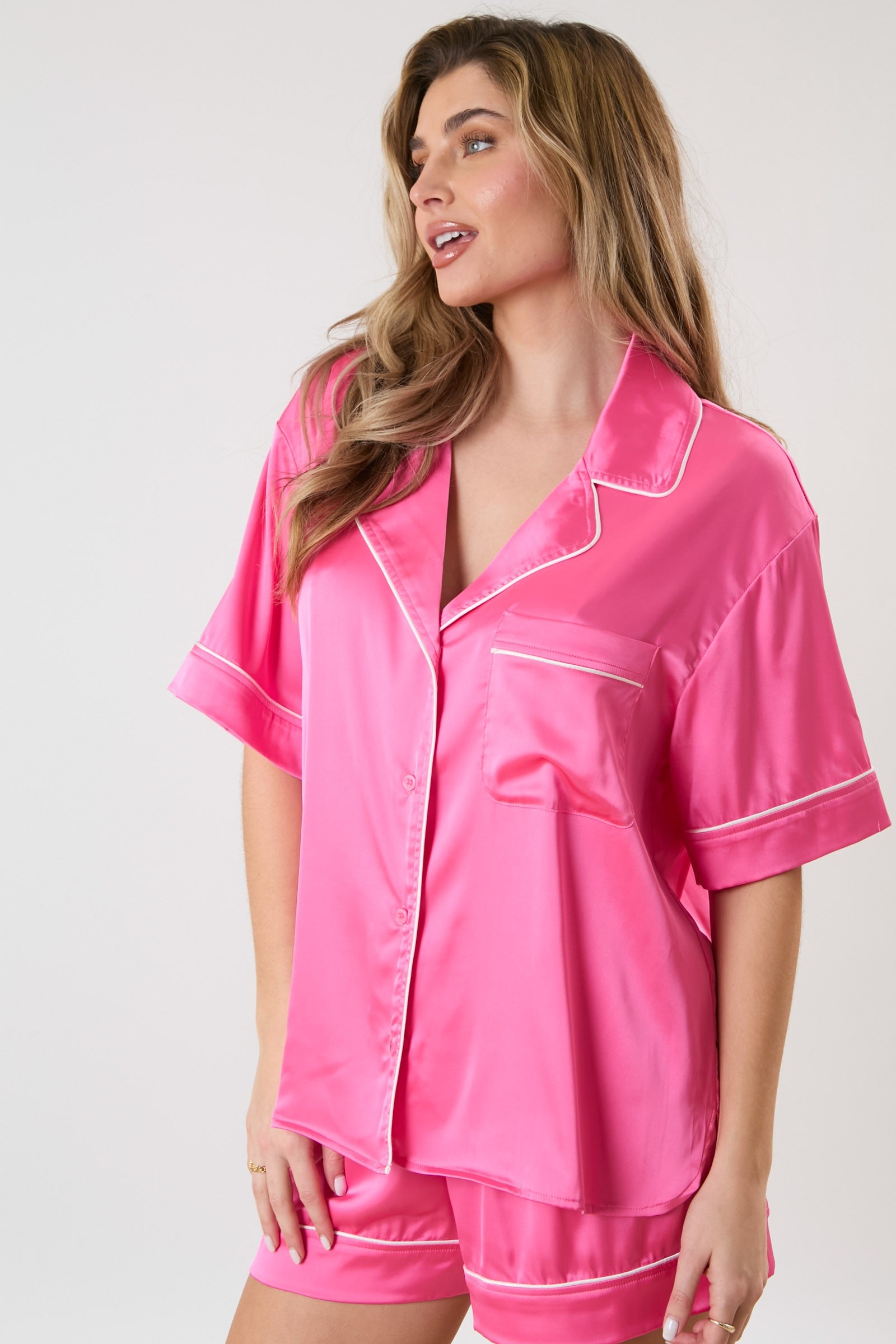 Bright pink Piping Satin Pajama Shirt. Short-sleeved, button-down with contrast piping and chest pocket. Paired with matching shorts. Sizes available: XS, S, M, L, XL.