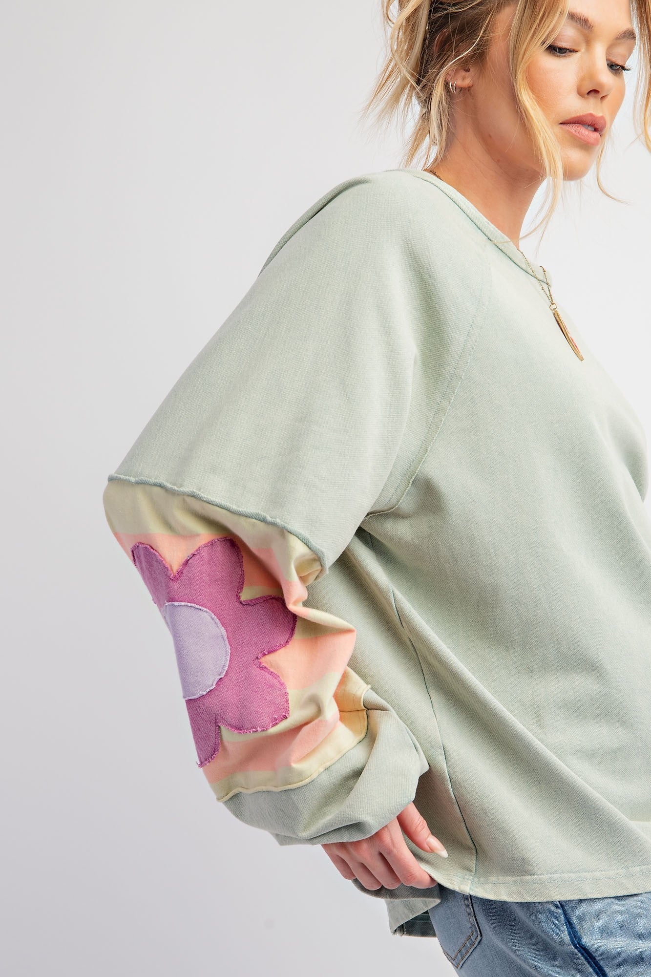 Light green Flower Patch Terry Knit Washed Pullover featuring a prominent pink and white flower design on the sleeve. Sizes available: S, M, L, XL.