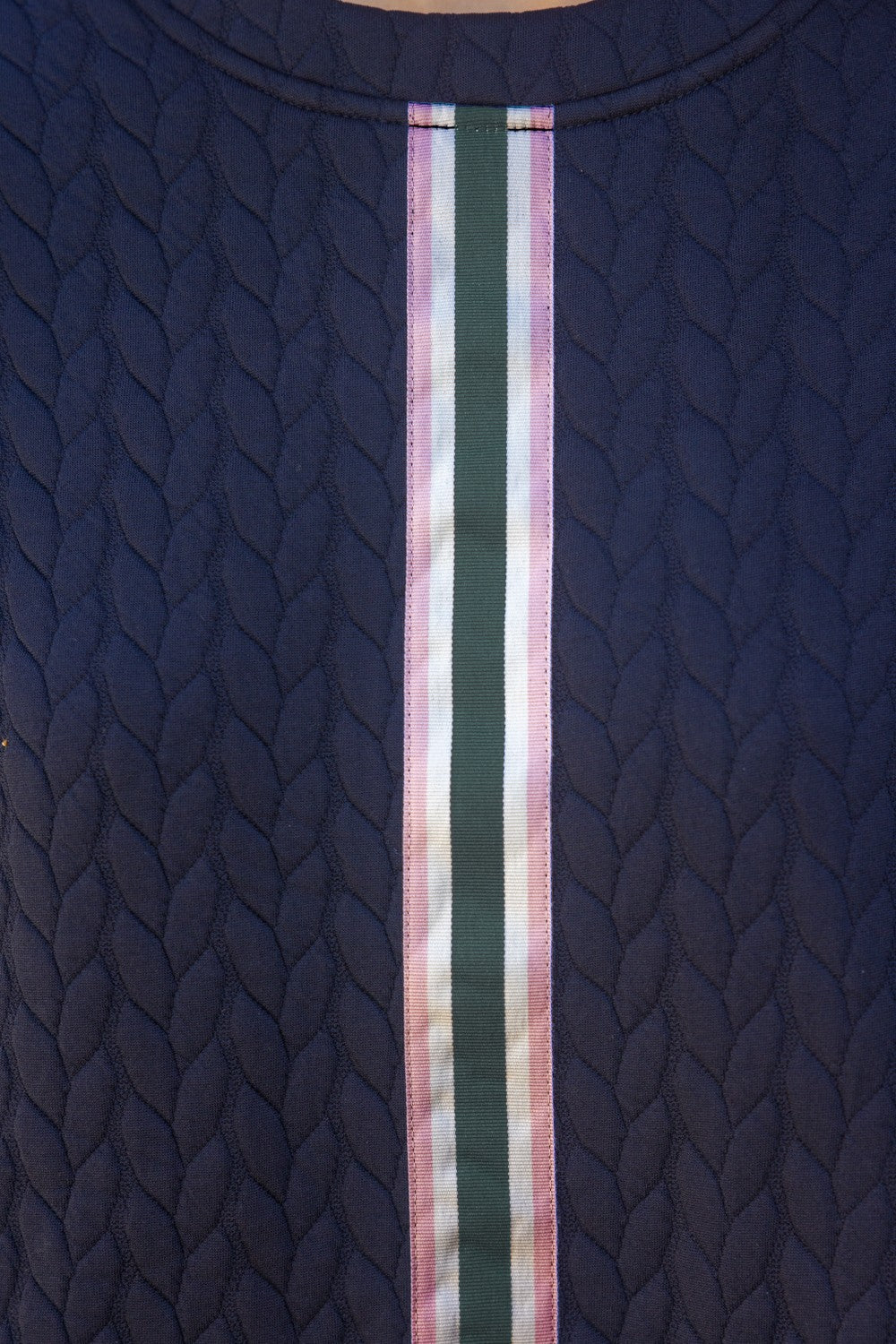 Close-up of Stripe Front Textured Knit Top in dark blue quilted fabric with a white, pink, green, and light purple vertical stripe. Comfy, stretchy fabric features a textured braided pattern and short puff sleeves. Available sizes: S, M, L.