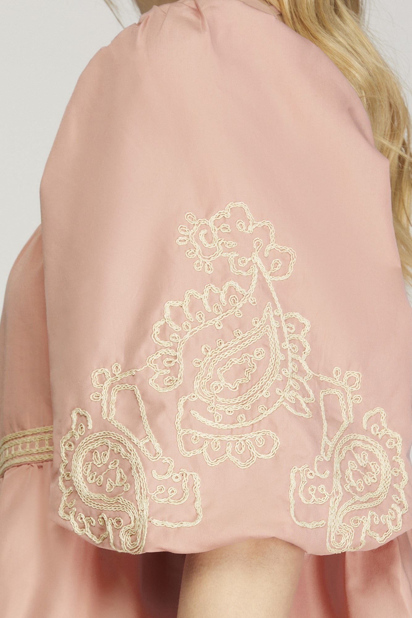 The Blossom Cascade Dress features intricate white embroidery with paisley and floral designs. It has elegant draping over the shoulder and puff sleeves. Available in sizes XS, S, M, L, XL.