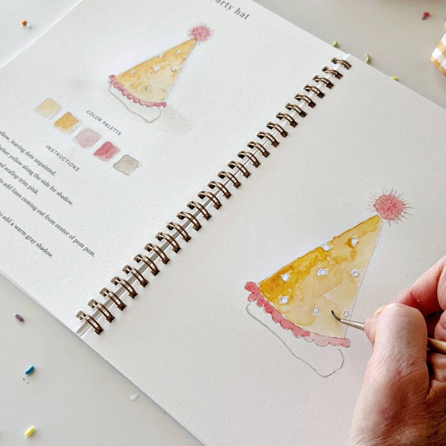 Celebrate watercolor workbook, spiral-bound, features step-by-step party hat painting instructions with a color palette guide. Available in multiple sizes.