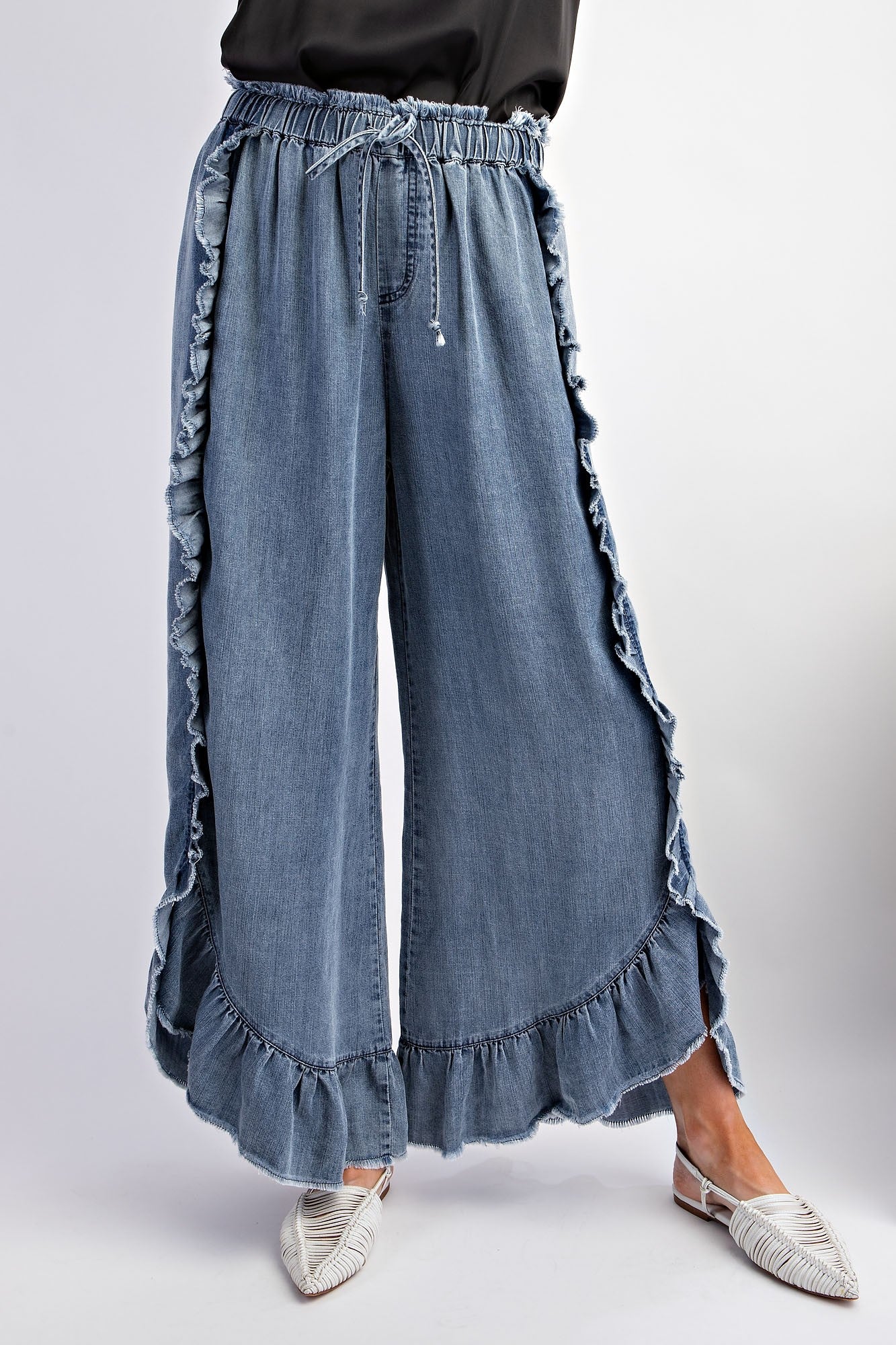 Washed Ruffle Chambray Loose Fit Pants in light blue with ruffled edging along sides and hem. Drawstring waist. Sizes available: XS, S, M, L.