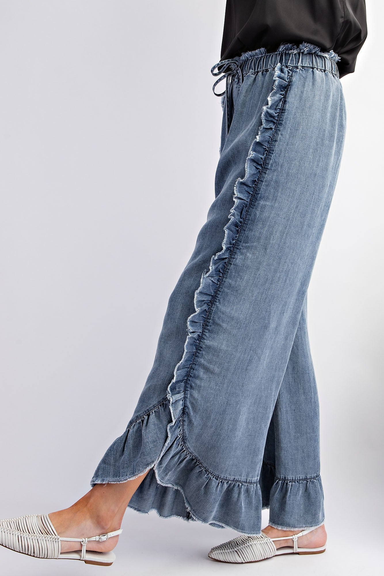 Washed Ruffle Chambray Loose Fit Pants featuring ruffled trim along side seam and hemline. Elastic waistband with drawstring. Sizes: S, M, L.