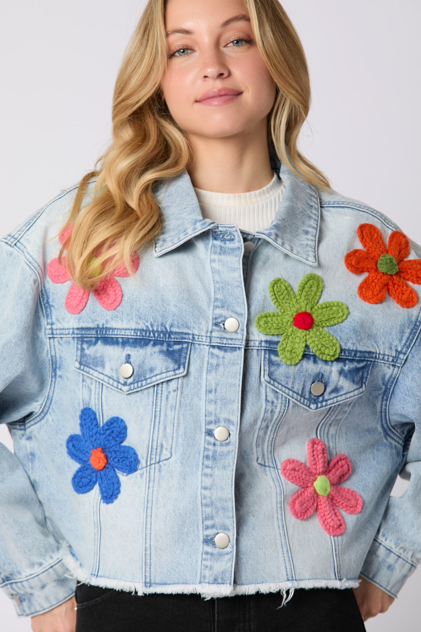 Oversized Denim Jacket with crocheted flowers in pink, green, blue, and orange on light blue denim. Features raw hem. Available in sizes S to XL.