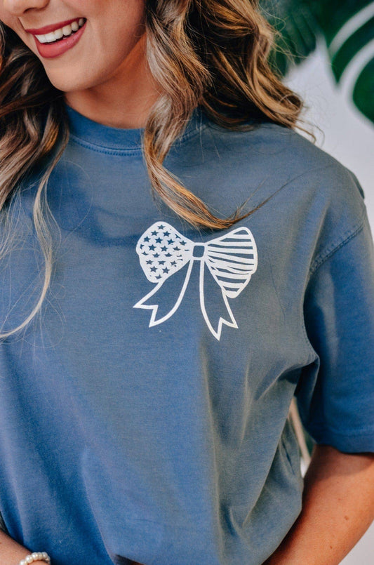 God Bless America Bow Tee: pigment-dyed denim blue shirt, white American flag bow graphic. Available in sizes S-XXL.