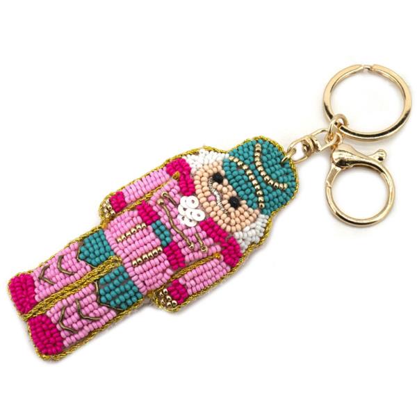 Christmas Spirit Keychain: Festive beaded keychain with a pink, green, and gold matador figure. Features a shiny gold clasp. Available in one size.