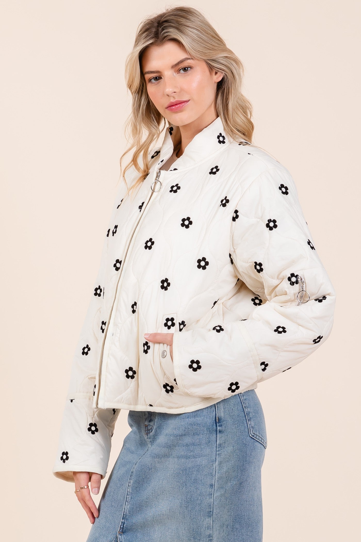 The Floral Blossom Quilted Jacket showcases black flower patterns on a quilted design. Available in sizes XS, S, M, L, and XL.