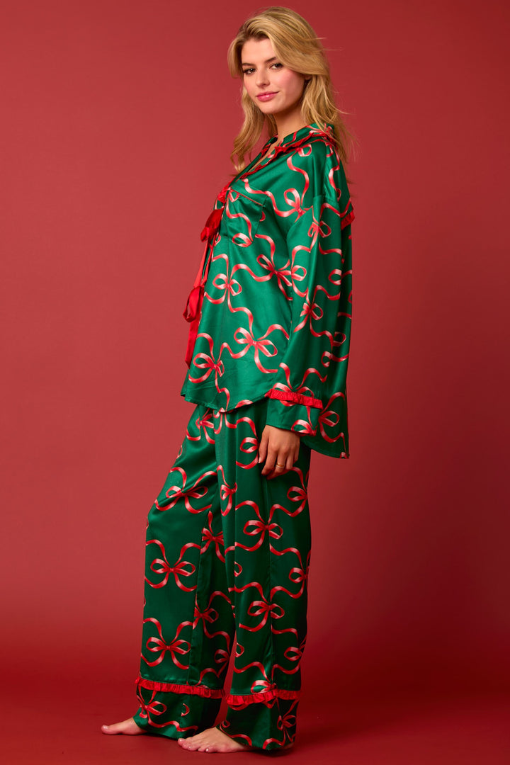 Green satin long-sleeve pajama set with red ribbon bow print, front-tie closure, and red ruffle trim.