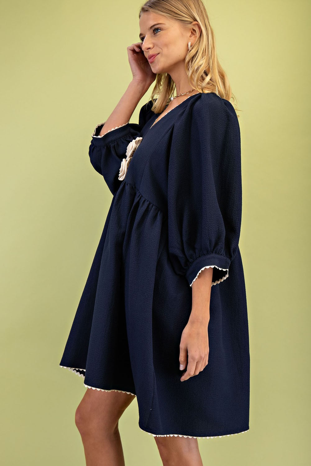 The Rosette Adorned V-Neck Mini Dress in navy blue features white ric-rac trim, a loose fit, and puffed three-quarter length sleeves. Available sizes: XS, S, M, L.