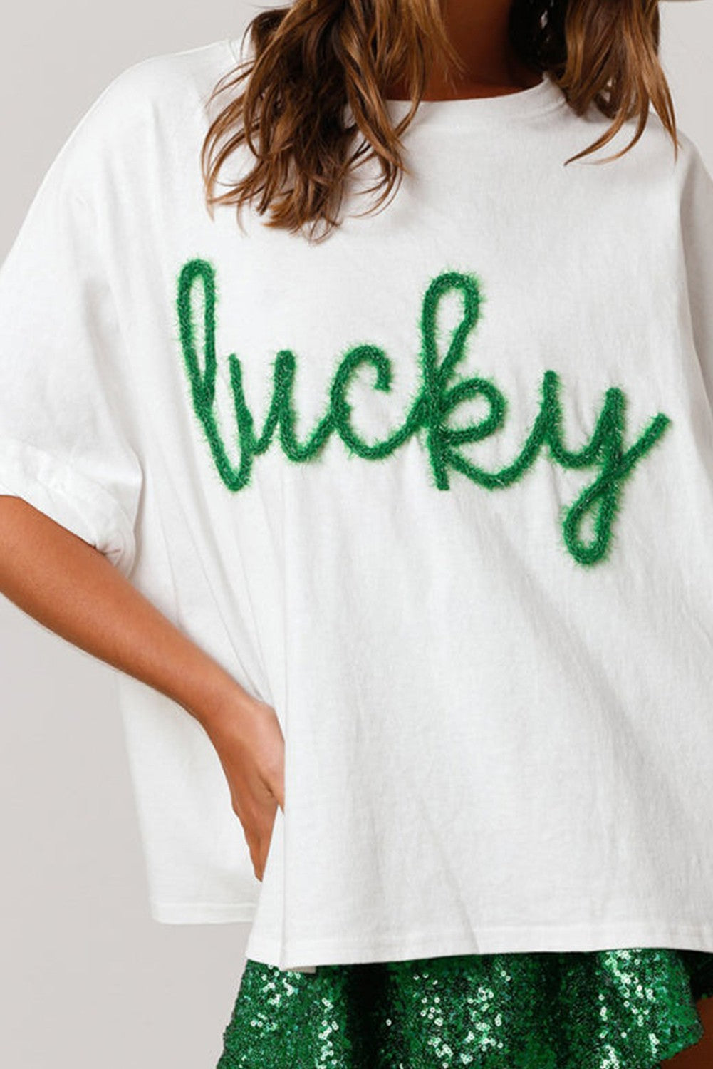 The Fuzzy Corded Lucky Graphic St. Patrick's Day T-Shirt features "lucky" in green lettering on a white shirt. Sizes: S, M, L, XL.