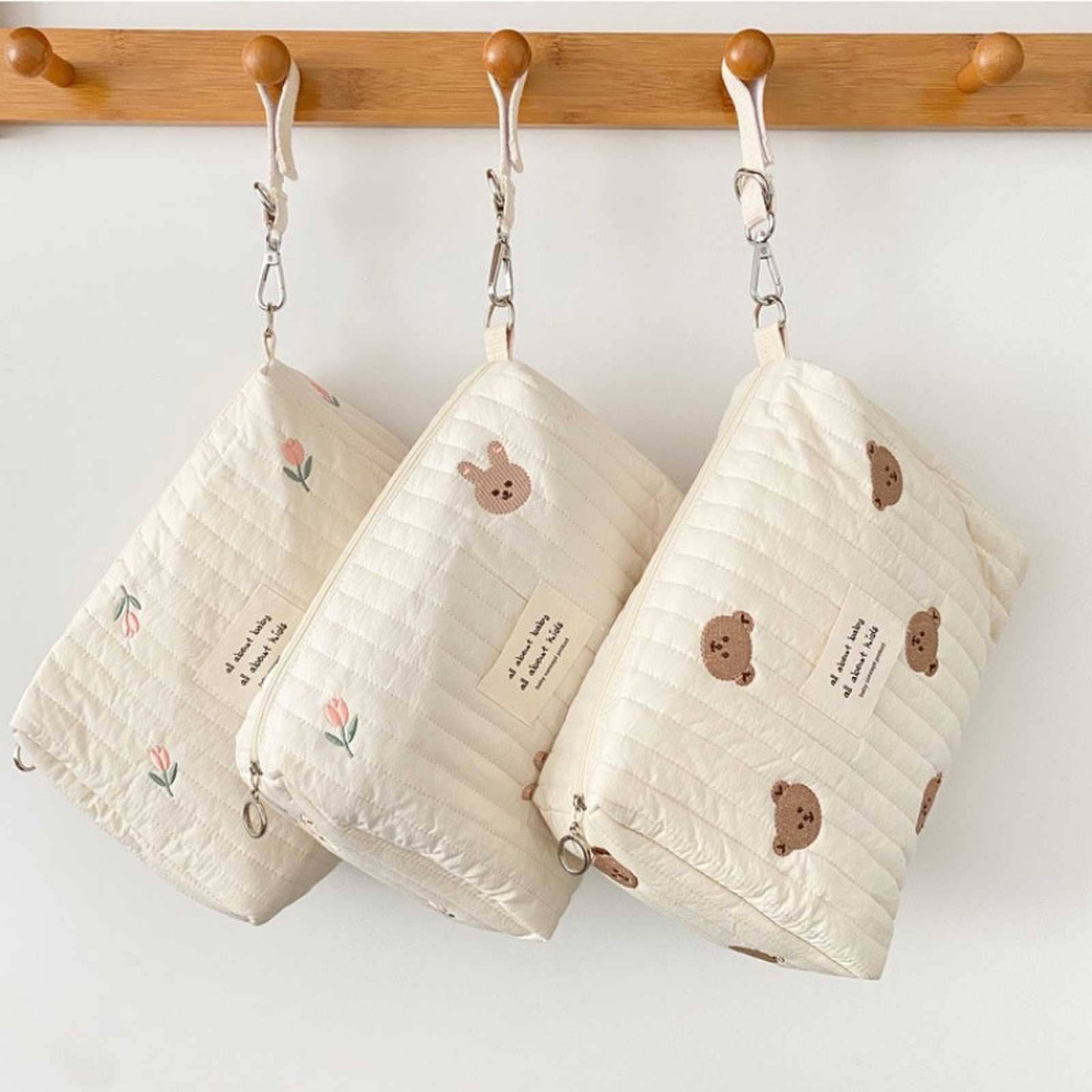 Three Little Bear Embroidered Diaper Bags, crafted from high-quality durable materials, hanging from wooden hooks by metal chains.