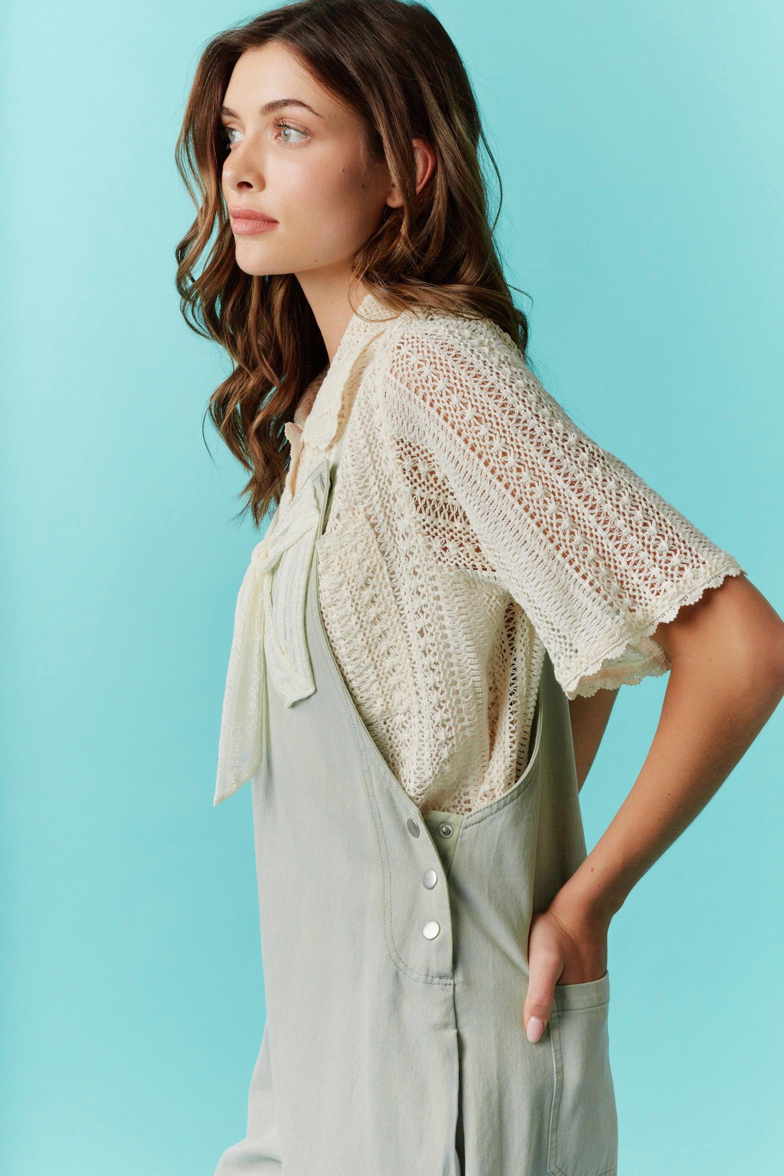 Twill Bow Overalls in cream with adjustable straps and pockets. Available in sizes XS–XL.