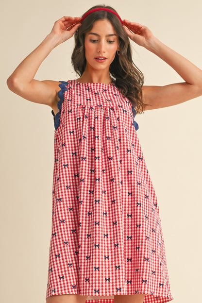 Miss Americana Bow Print Dress in red and white gingham with blue scalloped trim and small floral motifs. Available in sizes XS–XL.