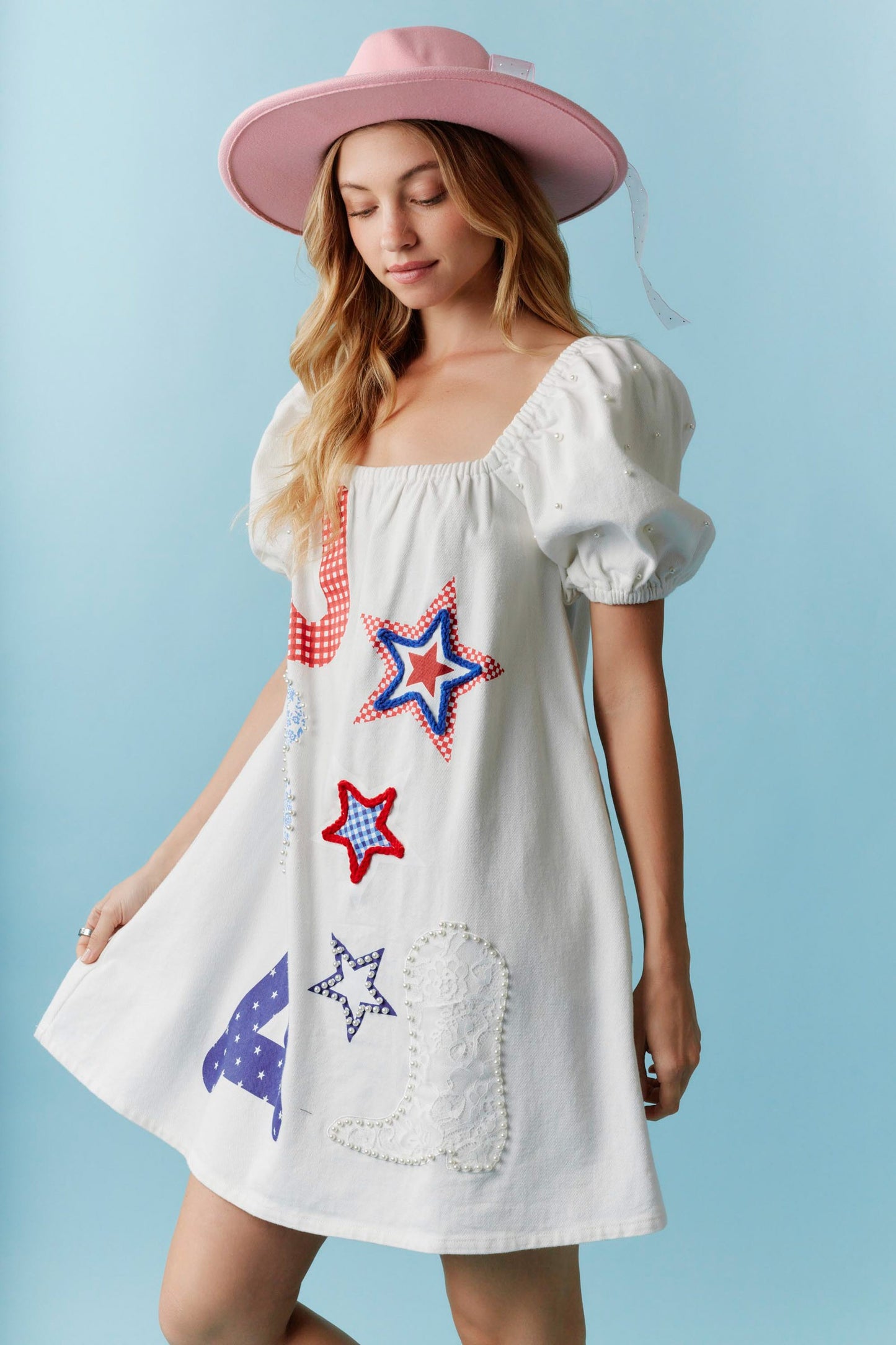 Star-Spangled Sweetheart Denim Dress with pearl details, red, blue, and white star and boot patches. Sizes available: XS, S, M, L, XL. Pink wide-brimmed hat sold separately. Ideal for USA print lovers and Independence Day.