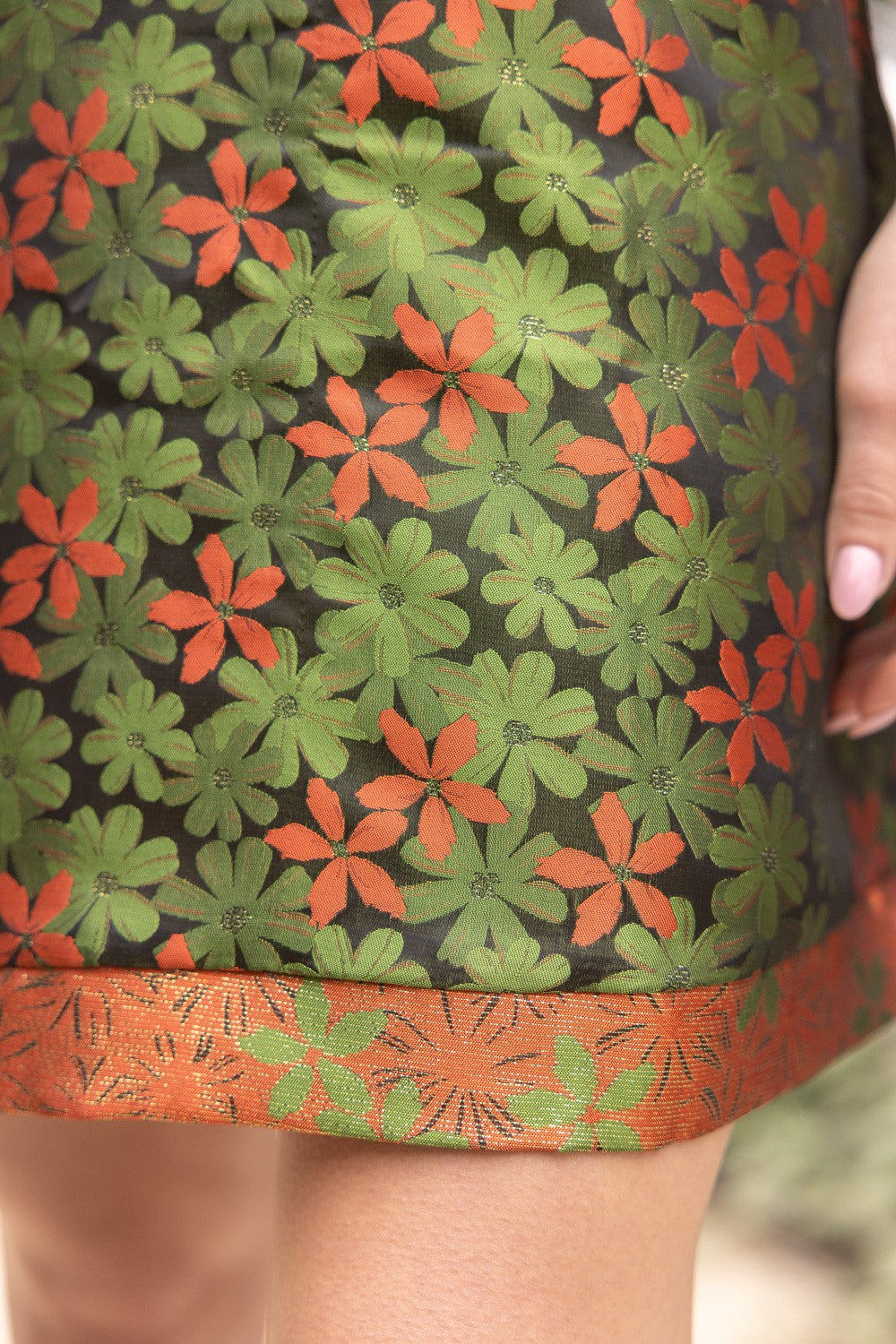 Close-up of skirt with green and orange floral sheer fabric, orange and gold embroidered hem. Available in sizes XS–XL.